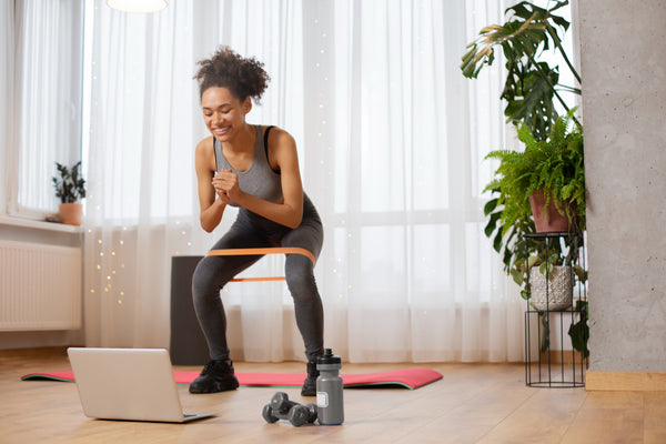 Woman exercising with resistance bands in a home setting, using a laptop.
