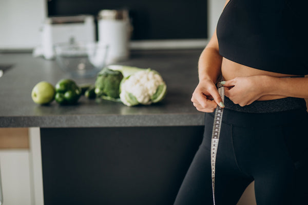 Person measuring waist with vegetables on a kitchen counter