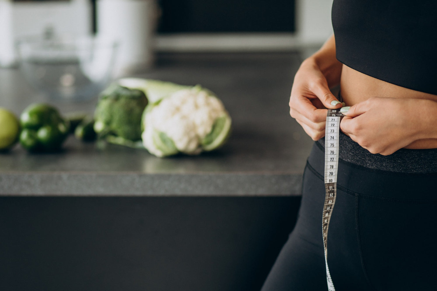 Person measuring waist with vegetables on a kitchen counter