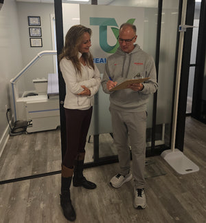 Two people standing in a room with a glass wall displaying a logo.