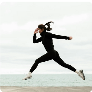 Person in black athletic wear performing a jump on a light background